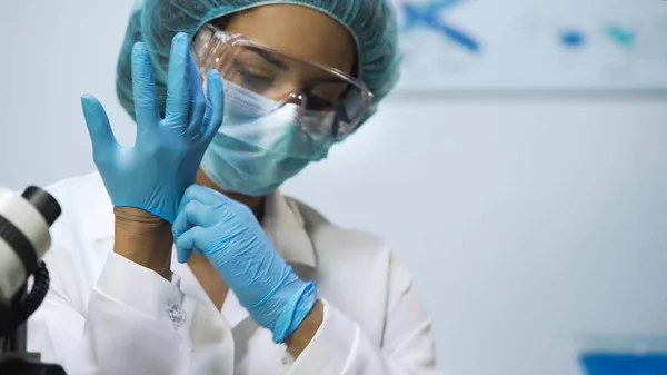 Березовая девушка надевает латексные перчатки в лаборатории, готовится к исследованиям — стоковое фото
