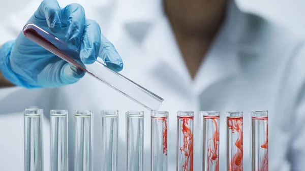 Laboratory assistant adding red dry test material into the tubes with water — Stock Photo, Image