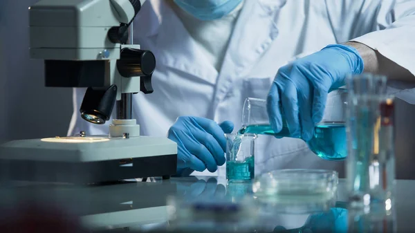 Assistente de laboratório derramando reagente líquido em copo para criar solução química — Fotografia de Stock