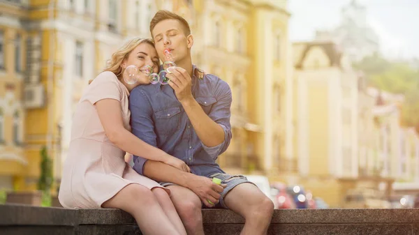 Despreocupado joven soplando burbujas de jabón, pareja disfrutando de la cita de verano en la ciudad — Foto de Stock