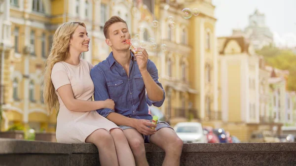 Verliebter Kerl macht Seifenblasen, verliebte Freundin sitzt neben ihm, Date — Stockfoto