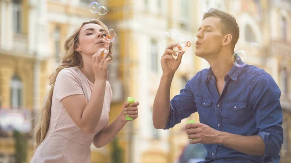 Playful couple blowing soap bubbles, enjoying time together, summer date — Stock Photo, Image