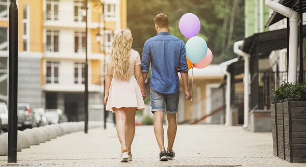 Lyckligt par promenader ner city street, innehav färgglada ballonger, romantisk datum — Stockfoto