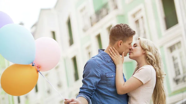 Dulce pareja besándose en la calle, cita romántica con globos de colores, felicidad —  Fotos de Stock