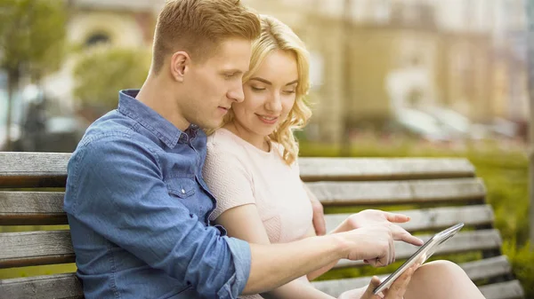Students in love sitting on bench, using laptop, choosing where to spend summer — Stock Photo, Image