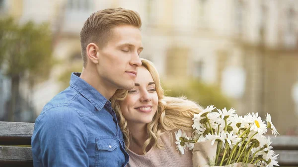 Verliebter Mann umarmt geliebte Freundin, glückliche junge Frau hält schöne Blumen — Stockfoto