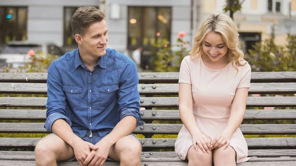Shy blonde girl smiling, attractive guy flirting with beautiful woman on bench — Stock Photo, Image