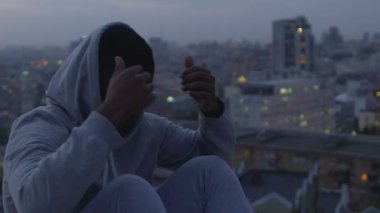 Çatının kenarında oturan ve gece şehir sahne bakıyor kazaklı kaydırma adam