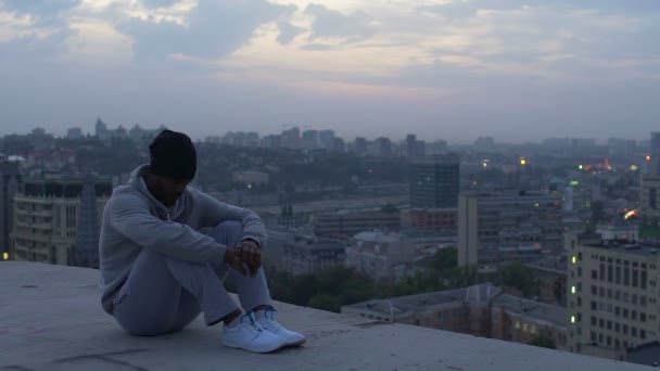 Guy pensively sitting on edge of skyscraper thinking about life, evening mist — Stock Video