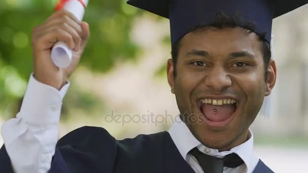 Estudiante de raza mixta en vestido académico francamente regocijándose en la graduación universitaria — Vídeo de stock