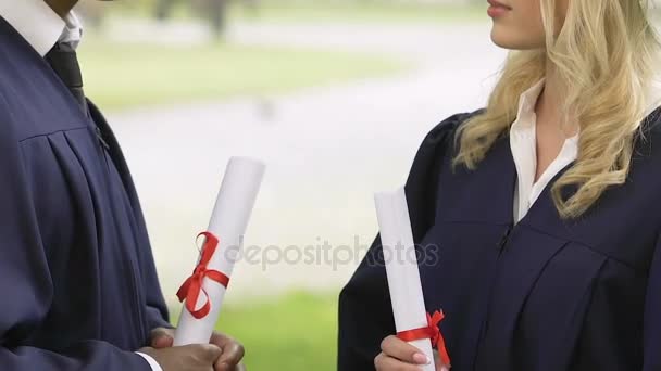 Un par de compañeros de clase multiétnicos diciendo adiós, dándose la mano después de la graduación — Vídeo de stock