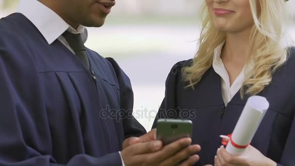 Αρσενικό απόφοιτος δείχνει θηλυκός συμμαθητής του πώς να χρησιμοποιήσετε την εφαρμογή για την αναζήτηση εργασίας — Αρχείο Βίντεο