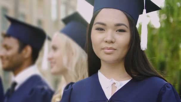 Ázsiai lány mosolyogva, pózol a kamera alatt a ballagási ünnepség akadémiai ruha — Stock videók