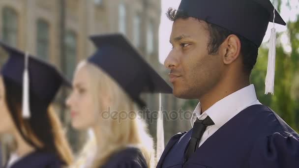 Stilig biracial kille leende poserar på kameran under examensceremoni — Stockvideo