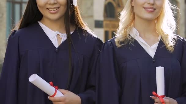 Dos hermosas chicas multiétnicas en vestido académico mostrando el signo de pulgar hacia arriba sonriendo — Vídeo de stock