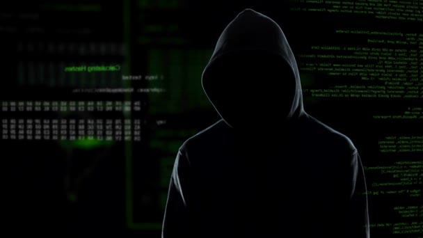 Ansigtsløs mandlig hacker i hættetrøje stående foran animeret computerkode – Stock-video