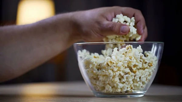 Közelkép a férfi kezét, figyelembe véve a popcorn tál asztalon, egészségtelen ételek rabja — Stock Fotó