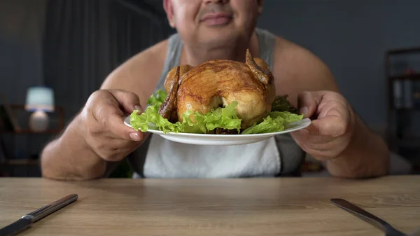 Homem com excesso de peso fedendo frango grelhado gorduroso com prazer, comida insalubre — Fotografia de Stock