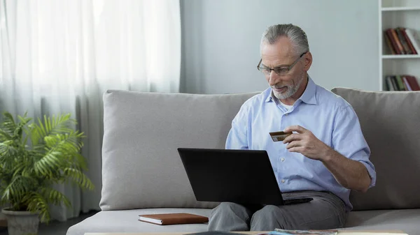 Attente senior man zittend op de Bank en het invoegen van kaartnummer op laptop — Stockfoto