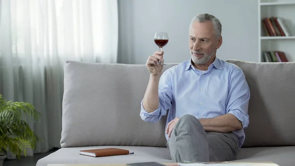Mann um die 50 sitzt auf Couch und verkostet Rotwein, riecht Aroma — Stockfoto