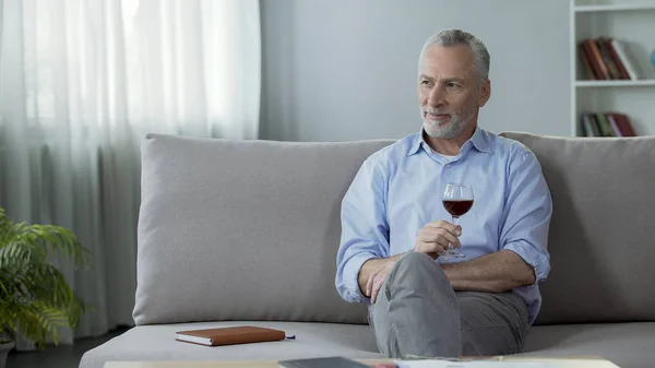 Glückliche erwachsene Person, die auf dem Sofa sitzt, Rotwein trinkt und über das Leben nachdenkt — Stockfoto