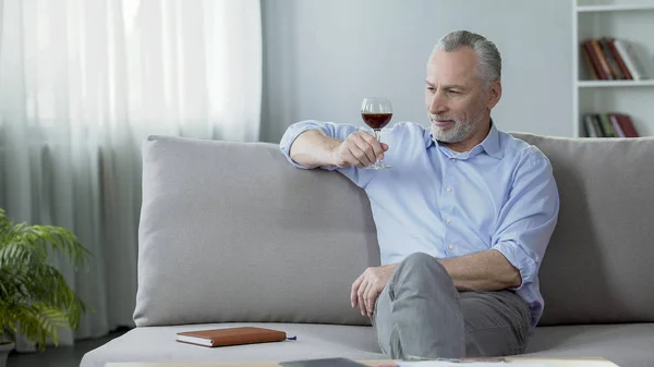 Pěkný starší muž, sedící na gauči a užívat si dokonalé víno chuť a aroma — Stock fotografie