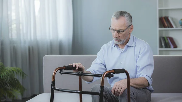 Senior mannen tittar på promenader ram, sitter på soffan på rehabiliteringscenter — Stockfoto