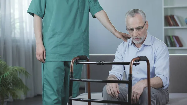 Sjuka äldre manliga sitter på soffan och tittar på walking ram med sorg — Stockfoto