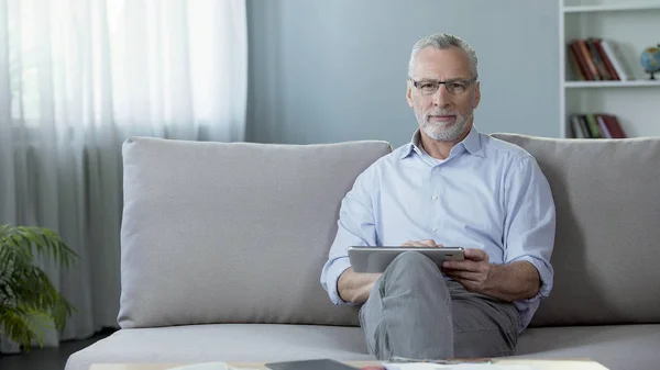 Hombre adulto guapo sentado en el sofá y desplazándose en la tableta, aplicación — Foto de Stock