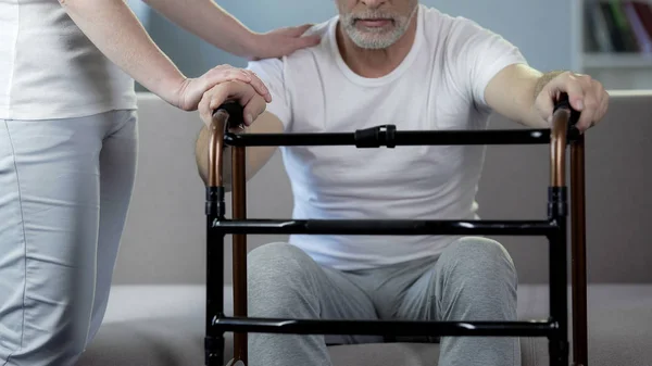 Sjuksköterska stödjande manlig pensionär hålla walking ram, rehabiliteringscenter — Stockfoto