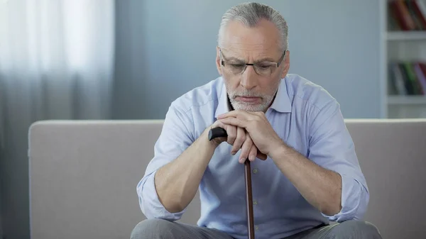 Triest mannelijke gepensioneerde zittend op de Bank, bedrijf wandelen frame en naar beneden te kijken — Stockfoto