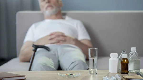 Medicamentos de pie sobre la mesa, abuelo enfermo y solitario durmiendo en el sofá — Foto de Stock