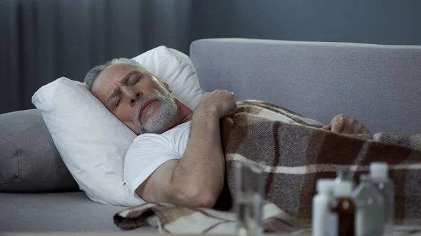 Férfi nyugdíjas alszik a kanapén, szenved a magas hőmérséklet, betegség — Stock Fotó