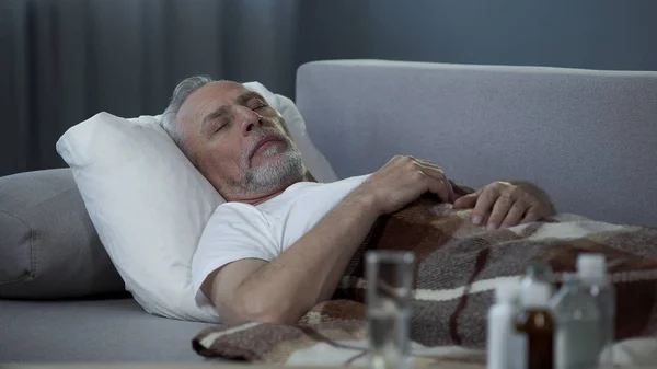 Beteg idősebb férfi alszik a kanapén, otthon, az asztalon álló gyógyszerek — Stock Fotó