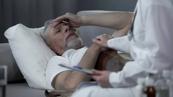 Hombre retirado acostado en la cama y quejándose médico sobre dolor de cabeza, alta temperatura —  Fotos de Stock