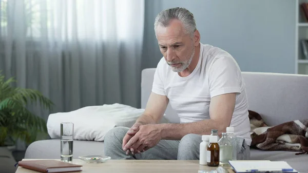 Lonely ill senior man sitting on couch and thinking about life, depression — Stock Photo, Image