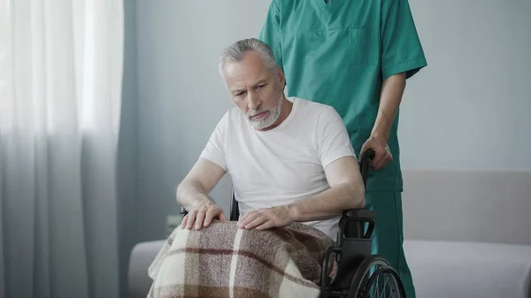Uomo anziano disabile seduto sulla sedia a rotelle, infermiere di sesso maschile che sostiene il paziente — Foto Stock