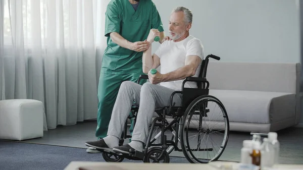 Hombre mayor levantando pesas, sentado en silla de ruedas en el centro de rehabilitación — Foto de Stock