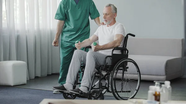 男性在轮椅上抽他虚弱的肌肉帮助护士, 康复 — 图库照片