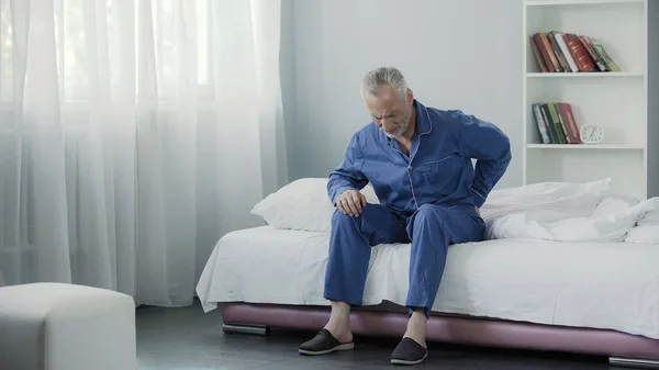 Пенсионер сидит в постели и чувствует ужасную боль в спине, здоровье и болезни — стоковое фото