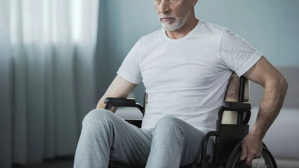 Hombre solitario sentado en silla de ruedas de nuevo a la cámara y mirando por la ventana — Foto de Stock