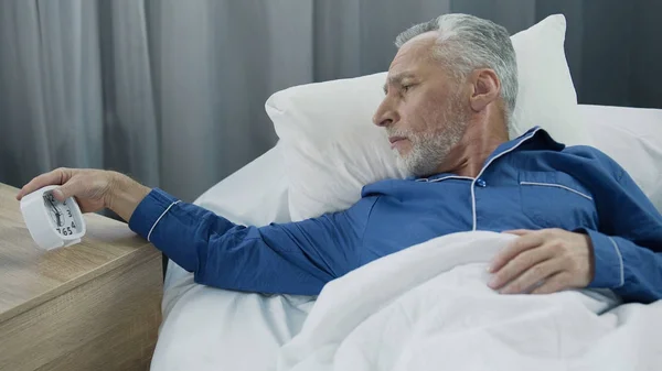 Anciano oyendo despertador, renuente a despertar, falta de sueño y energía —  Fotos de Stock