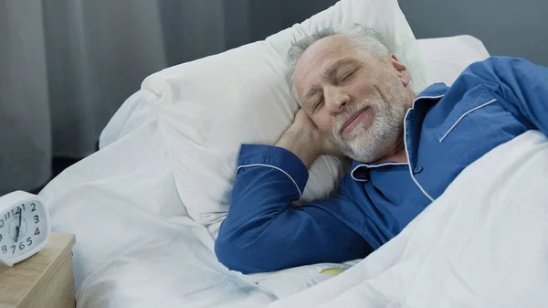 Homem sênior sorrindo enquanto dormia de manhã, aposentado satisfeito deitado na cama — Fotografia de Stock