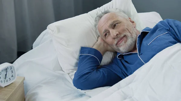Un bărbat în vârstă se trezește și zâmbește după un somn confortabil și sănătos — Fotografie, imagine de stoc