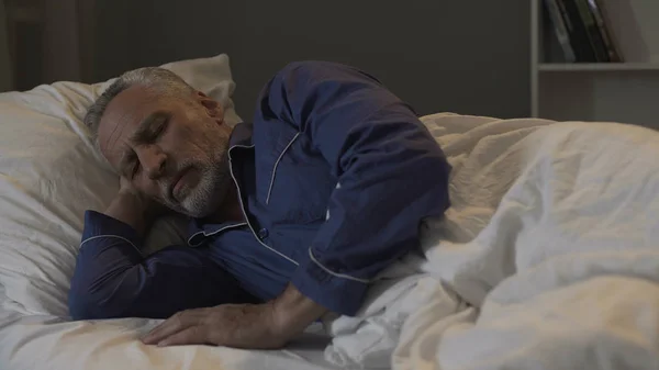 Старий чоловік лежить у ліжку і спить, час відновлення і здоровий сон, ніч — стокове фото