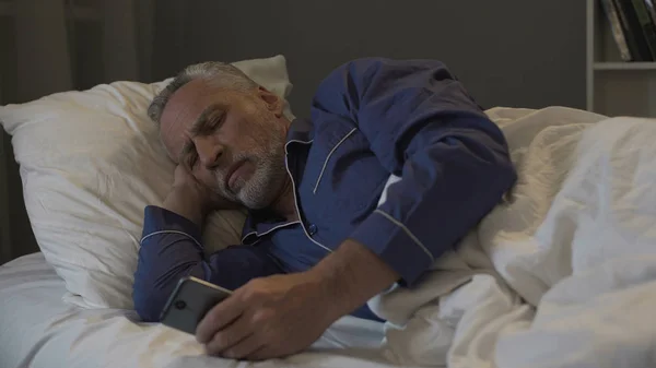 Adicto a la aplicación de desplazamiento del hombre retirado smartphone en lugar de dormir —  Fotos de Stock