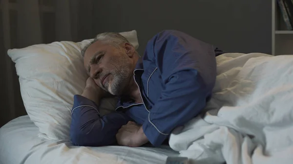 Grauhaariger Mann liegt im Bett und leidet unter Schlaflosigkeit, Depressionen und Gesundheit — Stockfoto