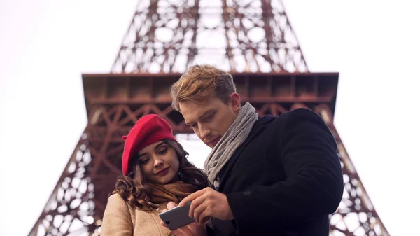 Turistas masculinos y femeninos en busca de destino en París en el mapa en la aplicación móvil — Foto de Stock