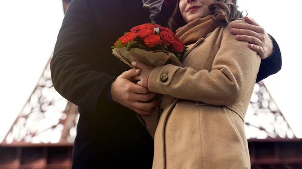 Мужчина нежно обнимает возлюбленную женщину с красивыми цветами в руках, романтика в Париже — стоковое фото