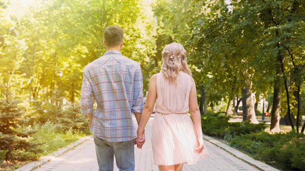 Красива молода пара, що прогулюється крізь засвічений яскраво-зелений парк, романтичне побачення — стокове фото